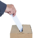 Businessman putting ballot in vote box on white background