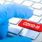 Hand with protecting glove and Keyboard with red key and COVID-19 message. Coronavirus concept